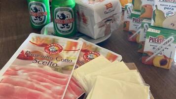 Una cesta de compras con latas de cerveza, queso empaquetado y bolsas de fruta.