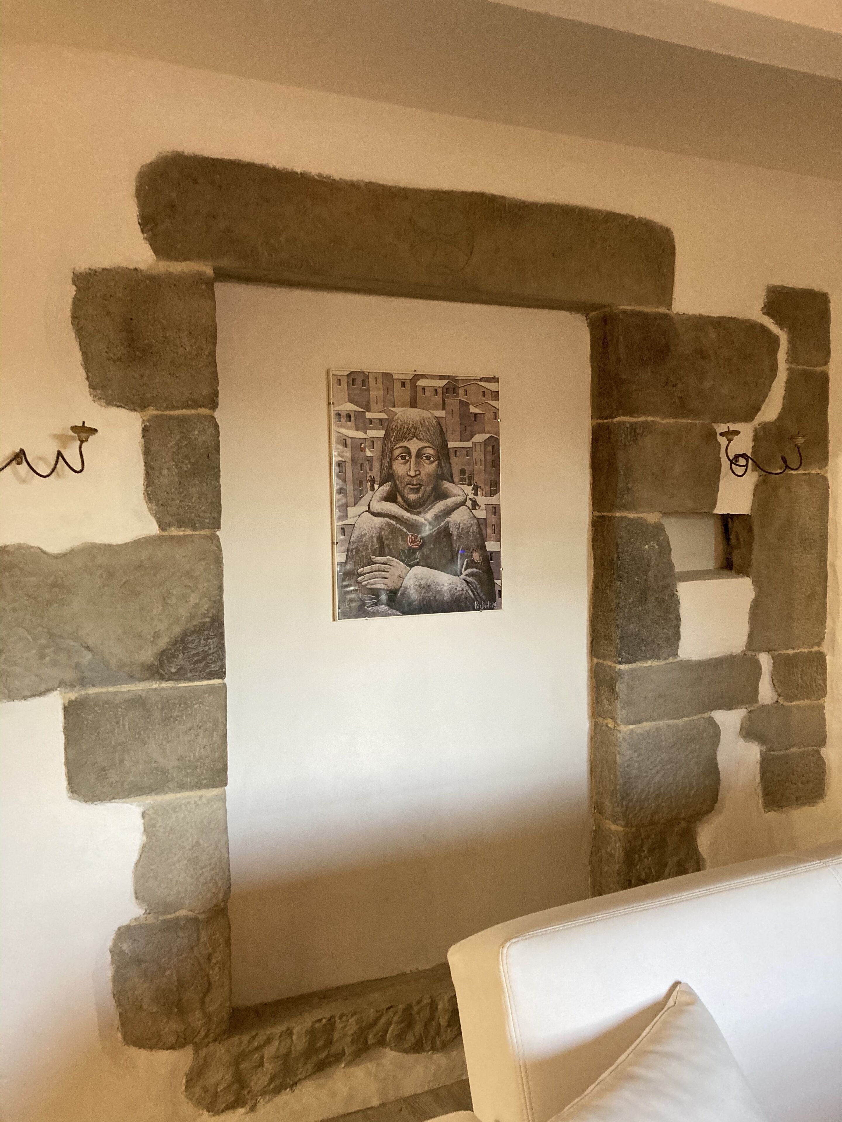 Un'opera d'arte incorniciata raffigura una persona con una veste e una rosa, inserita in un arco in pietra sopra un divano bianco.