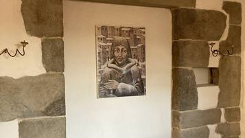 Un'opera d'arte incorniciata raffigura una persona con una veste e una rosa, inserita in un arco in pietra sopra un divano bianco.