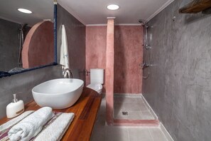 A bathroom with a large white sink, a wooden vanity, a mirror, a towel, a toilet, and a shower area.