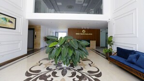 A spacious lobby with a reception desk, a large potted plant, a blue sofa, and a decorative floor pattern. - Minh Quan Building (Vinh Phuc)