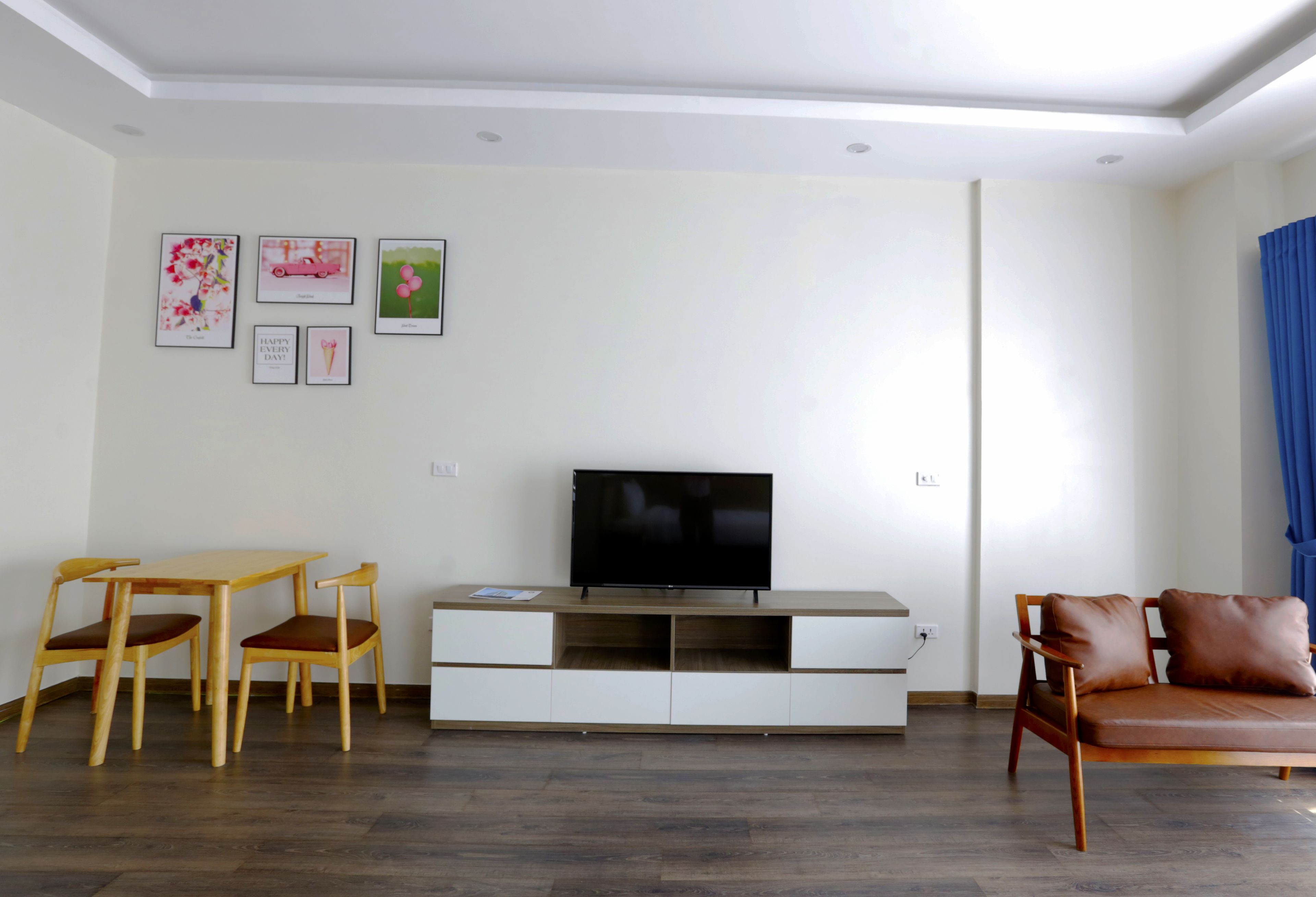 A living room with a TV, wooden chairs, a sofa, and a white entertainment unit.