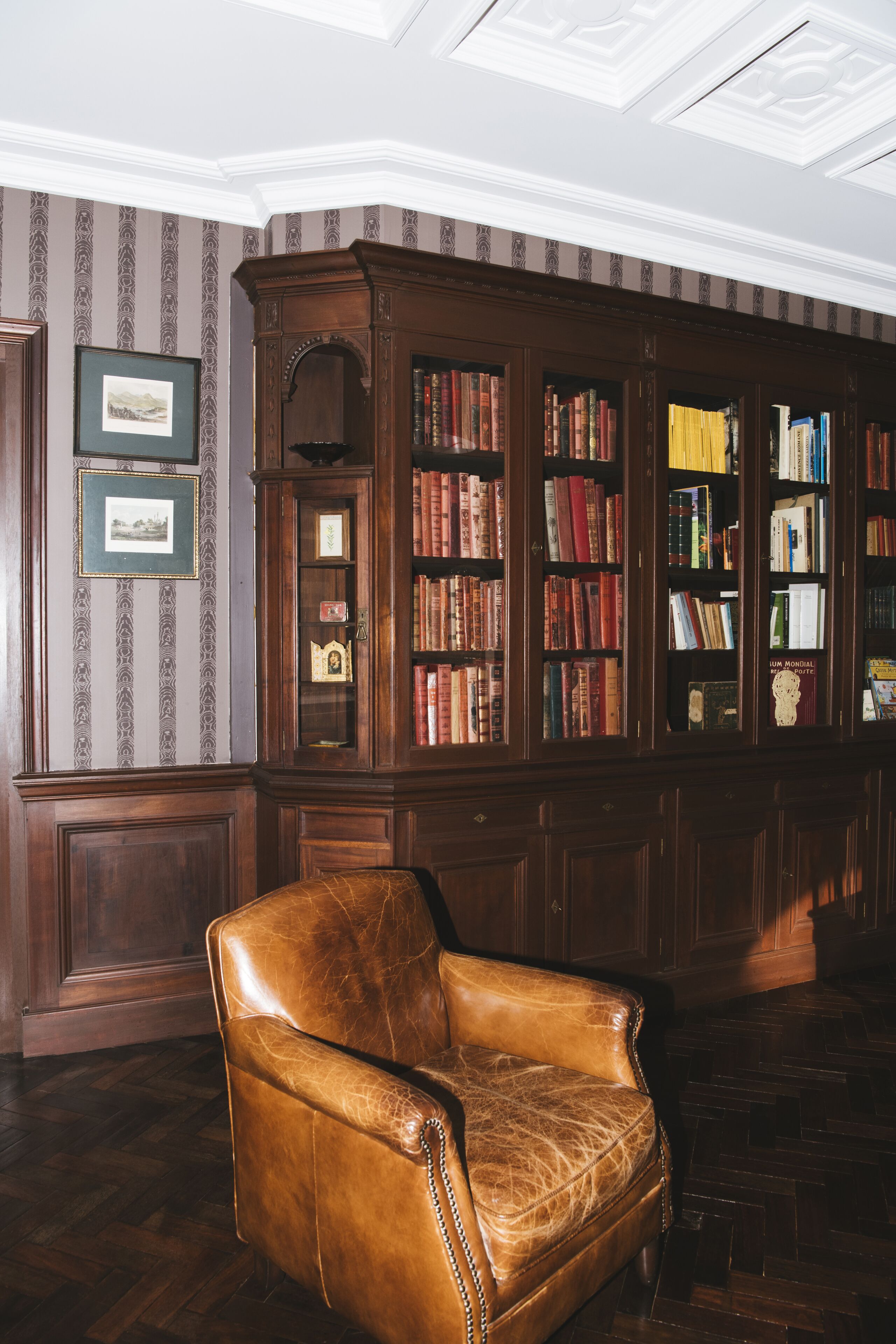A library with a leather armchair, wooden bookshelves, and patterned wallpaper.