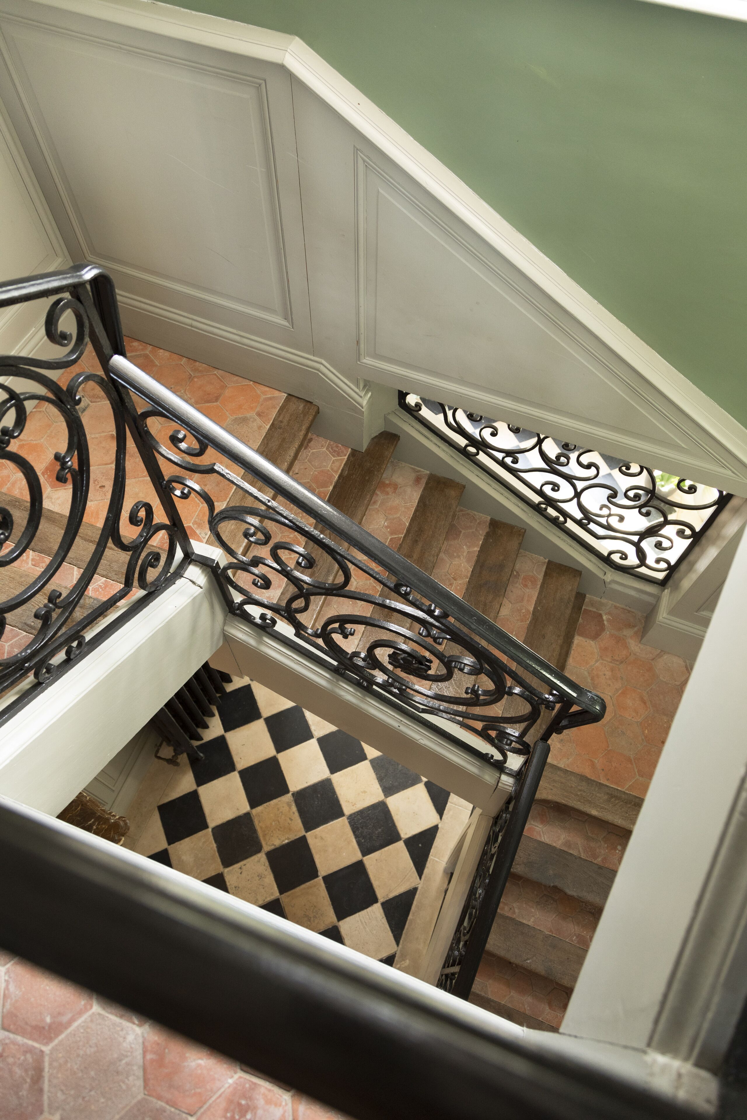 A staircase with black and white checkered flooring, white walls, and black wrought iron railings.