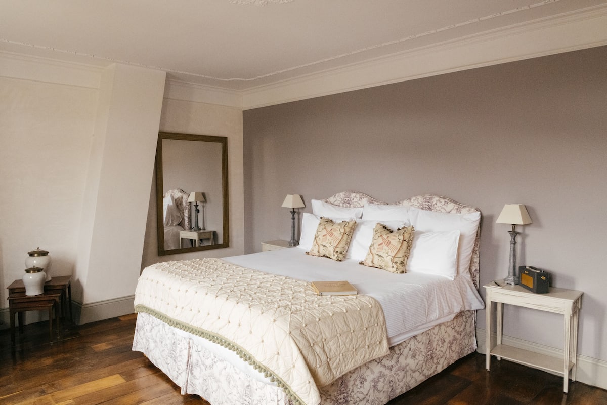 Un dormitorio ordenado con una cama grande, mesitas de noche, un espejo y una lámpara.