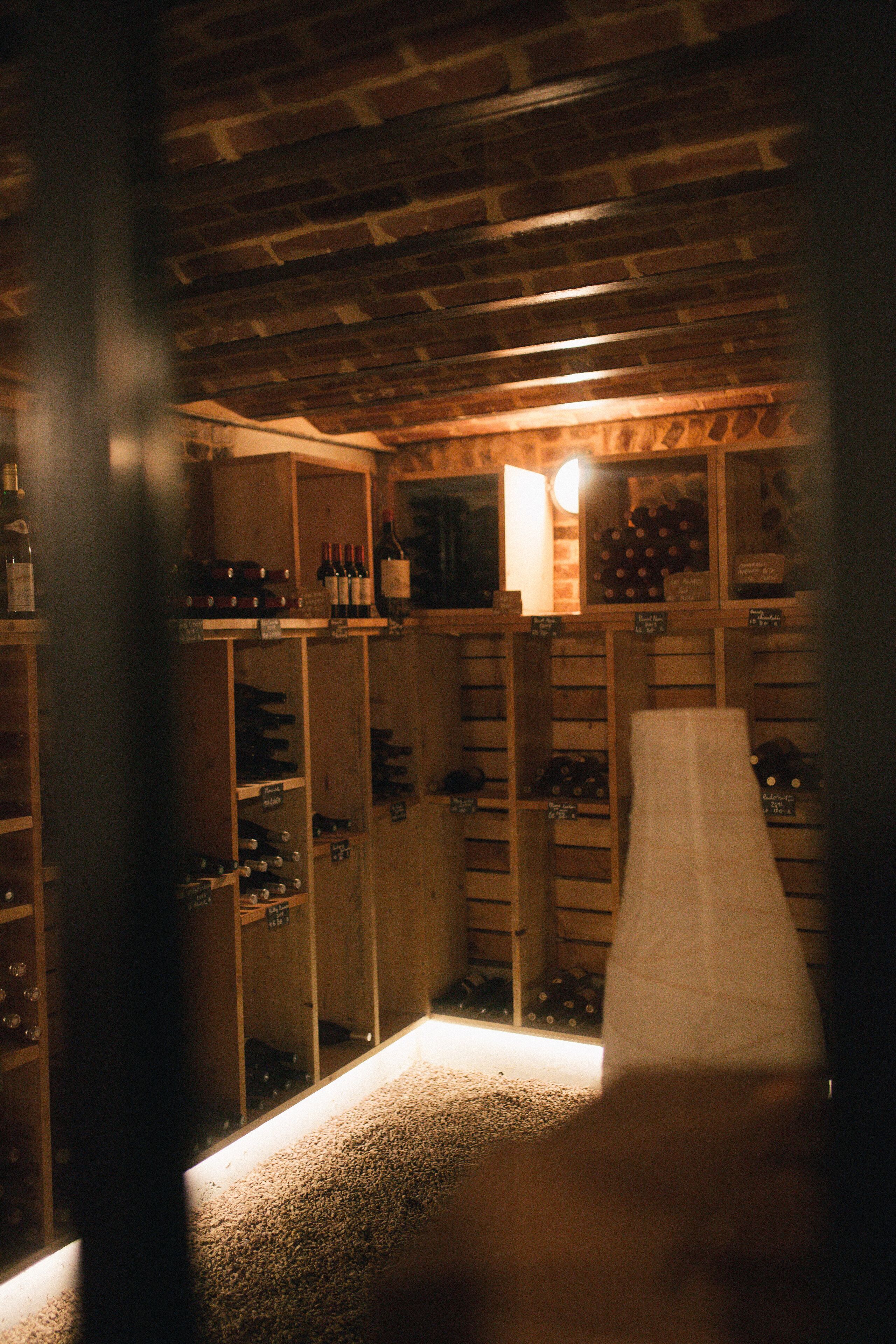 A dimly lit wine cellar with wooden shelves and racks holding bottles.