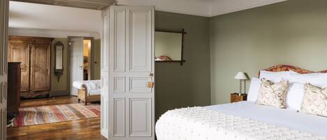 A bedroom with a large bed, a wooden wardrobe, and a door leading to another room.