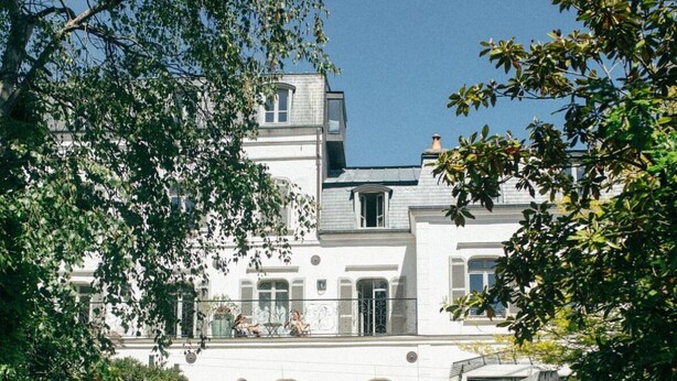 Un grand bâtiment blanc, doté de nombreuses fenêtres et d’une entrée en briques.