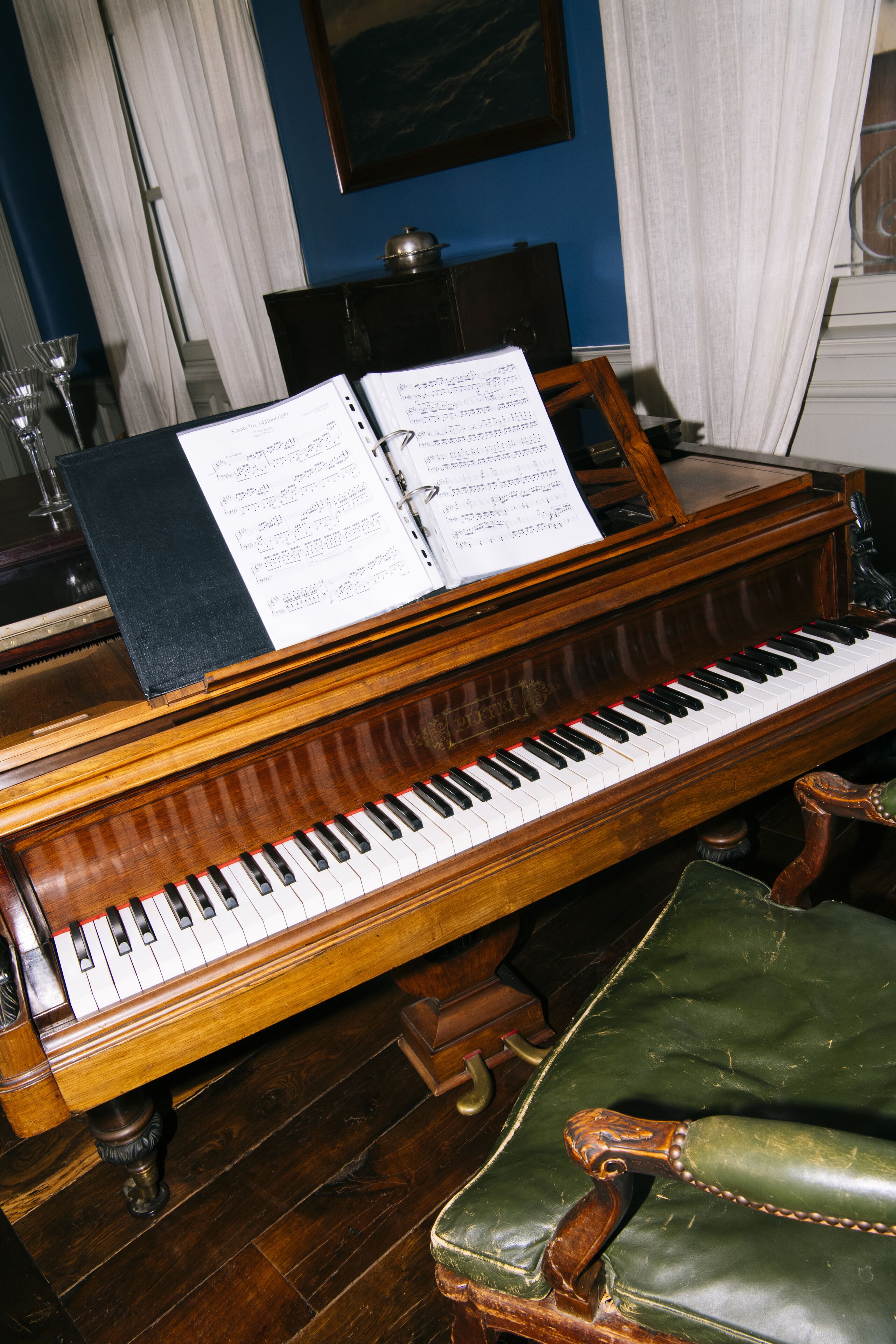 A grand piano with sheet music, a wooden bench, and a dark wooden cabinet in a room with blue walls.