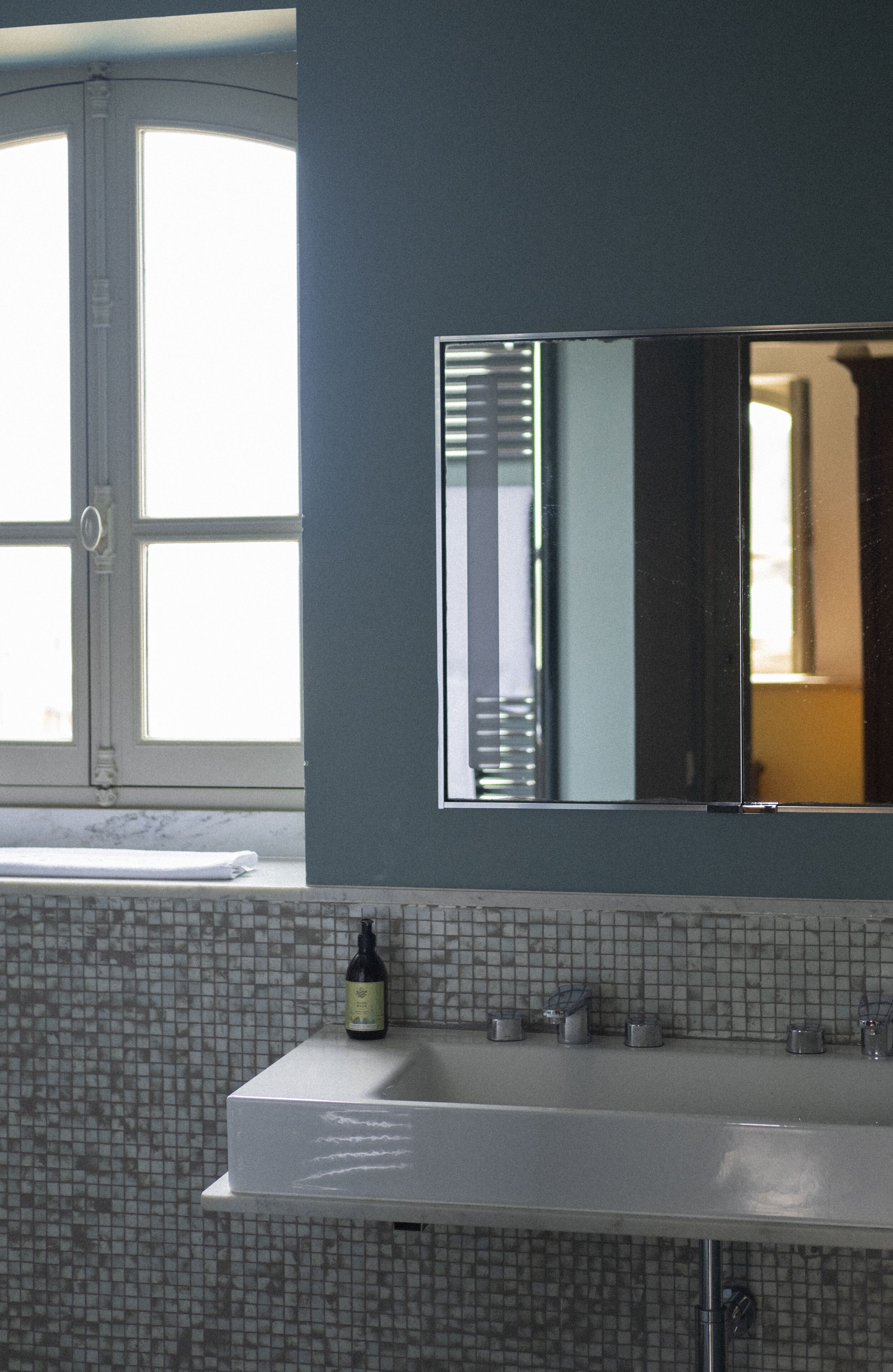A bathroom with a large mirror, a white sink, and a window with blinds.