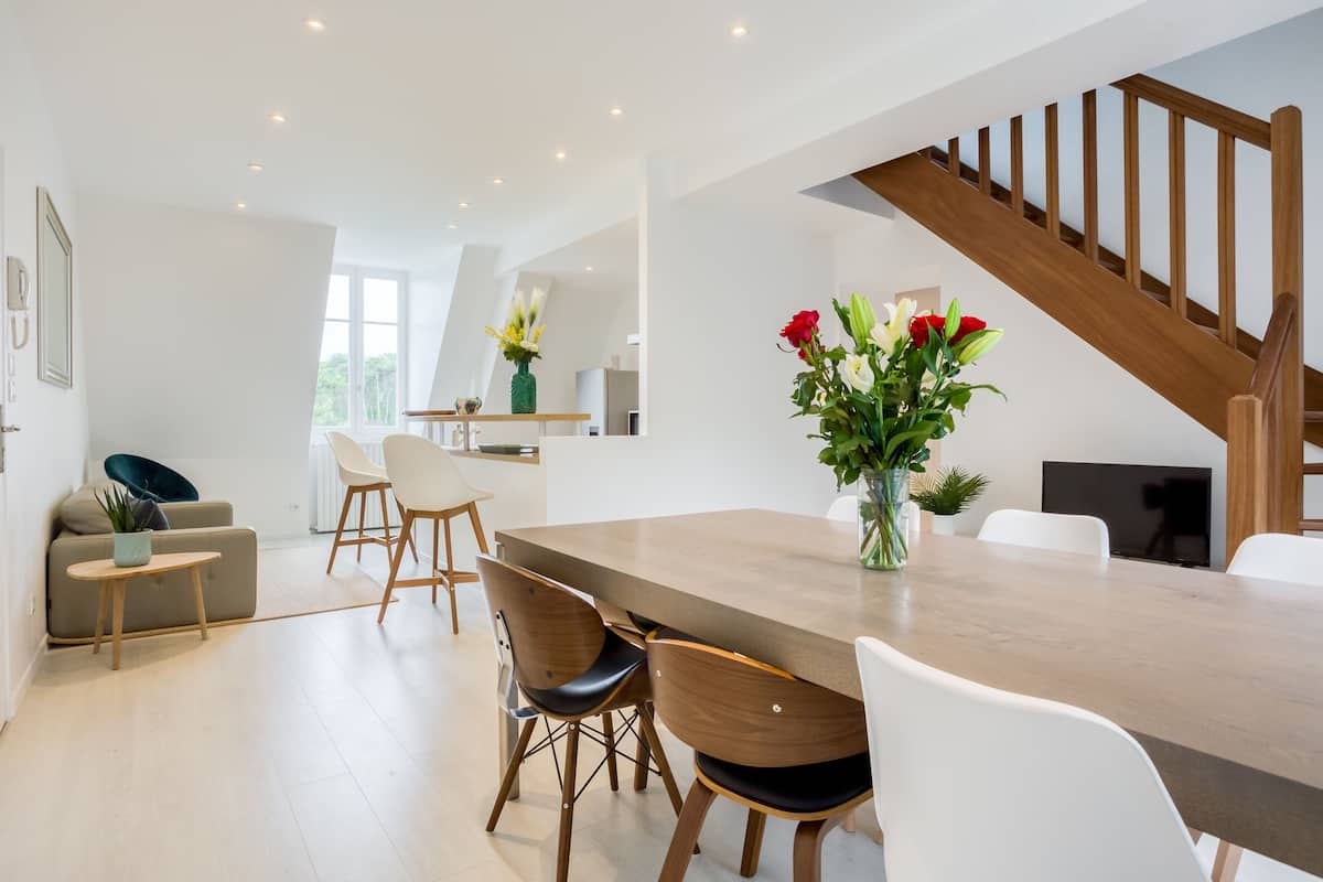 A modern kitchen with a dining area, wooden staircase, and a view of the outdoors.