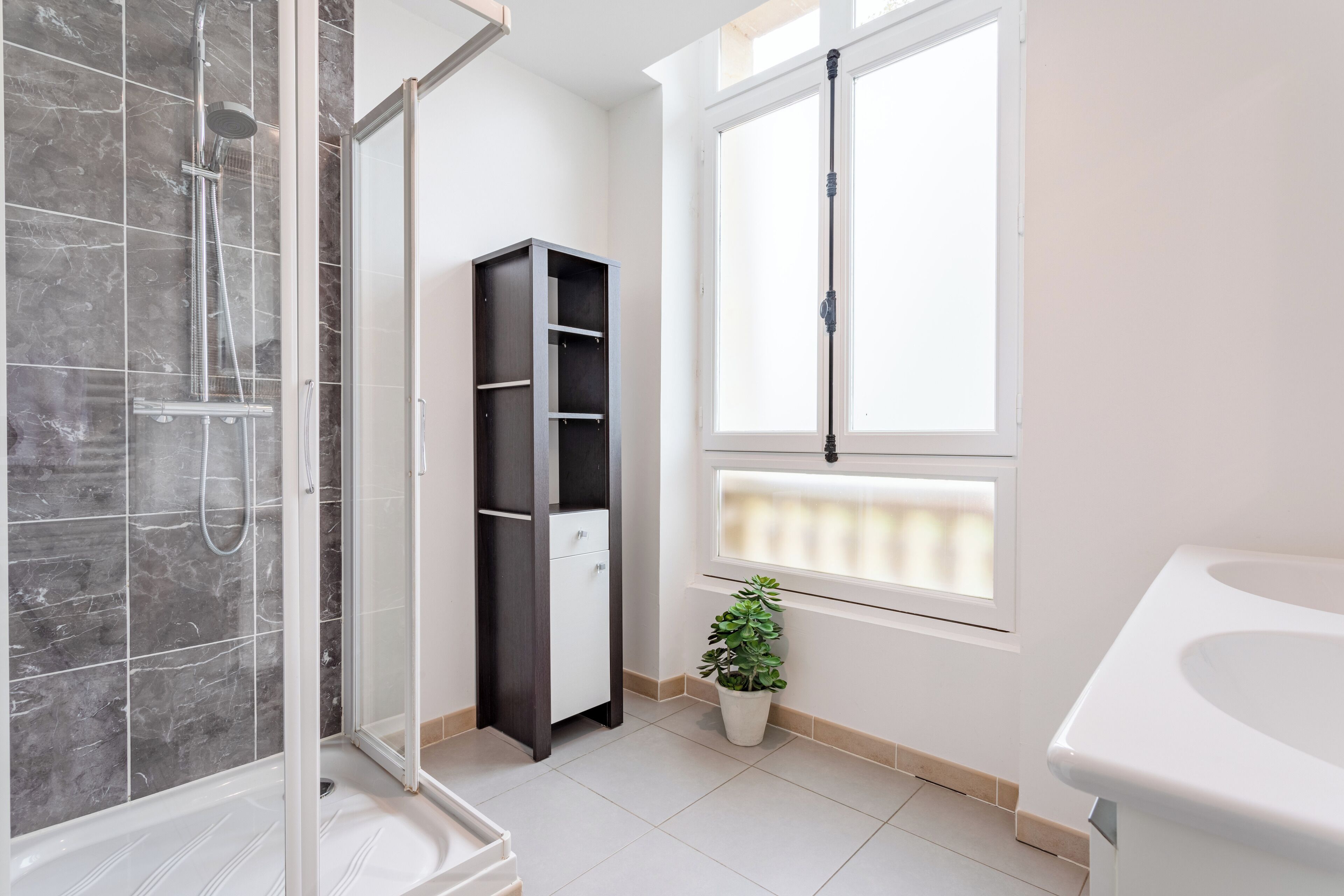 A bathroom with a shower, a toilet, a sink, a window, and a potted plant.