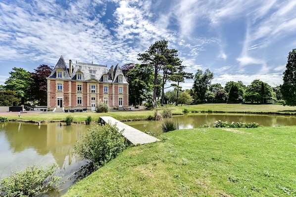 A large, historic building with a pond and a wooden bridge. - Château Côte de Nacre (Ver-sur-Mer)