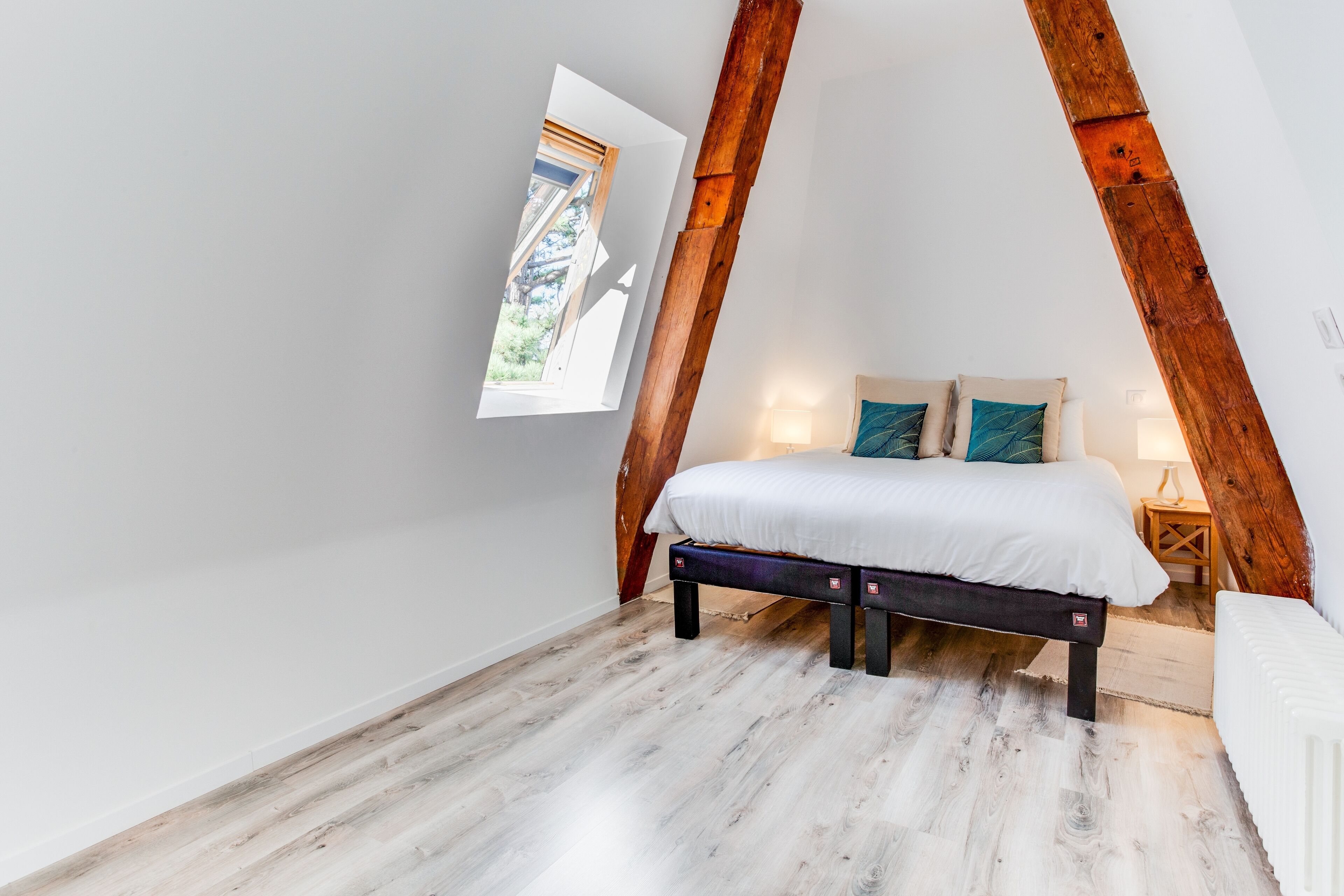 A bedroom with a sloped ceiling, a bed with white bedding, a nightstand, and a small window.