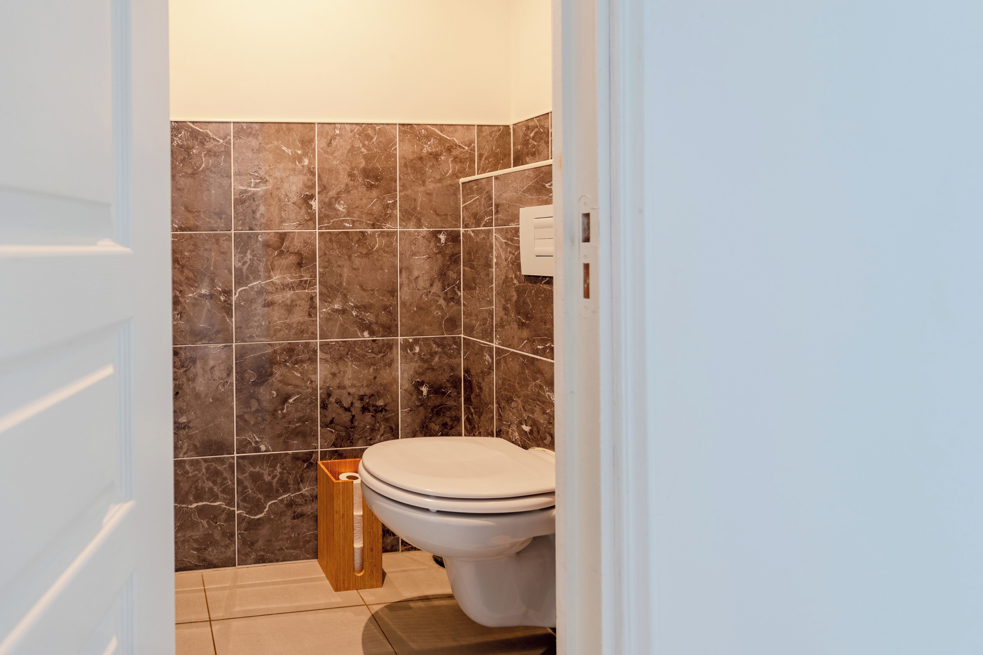 A bathroom with a toilet, marble tiles, and a wooden cabinet.