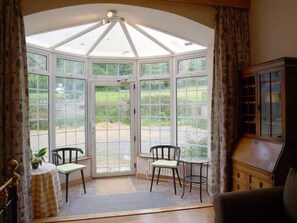 A conservatory with a glass roof, two chairs, a small table, and a cabinet. - Ross House Equestrian Holidays (Ross)
