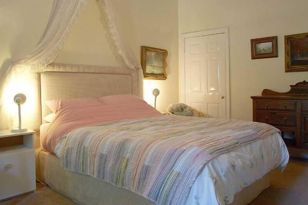 A bedroom with a bed, a nightstand, a dresser, a door, and a painting on the wall.
