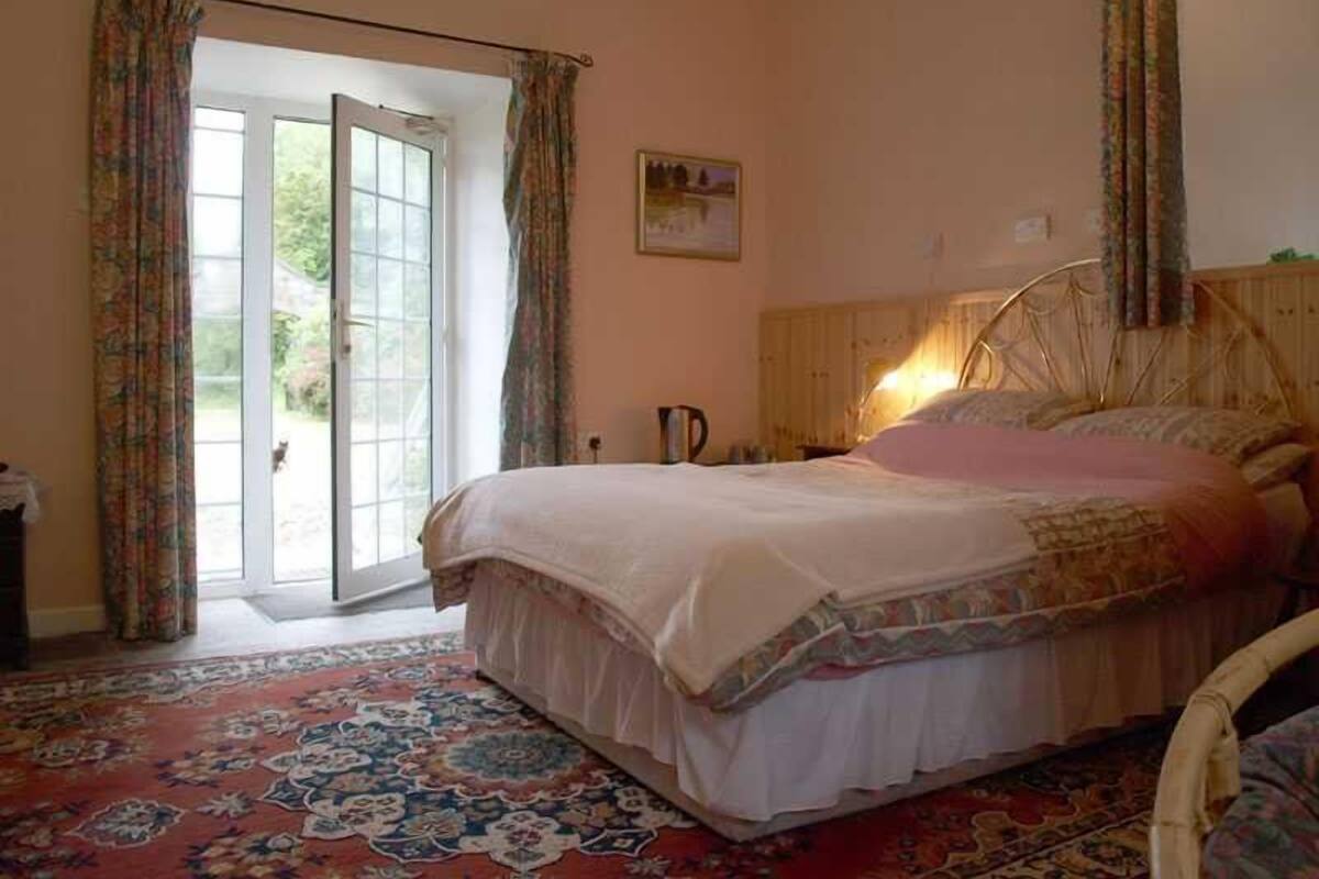 A bedroom with a bed, a wooden headboard, a patterned rug, and a door leading to a balcony.