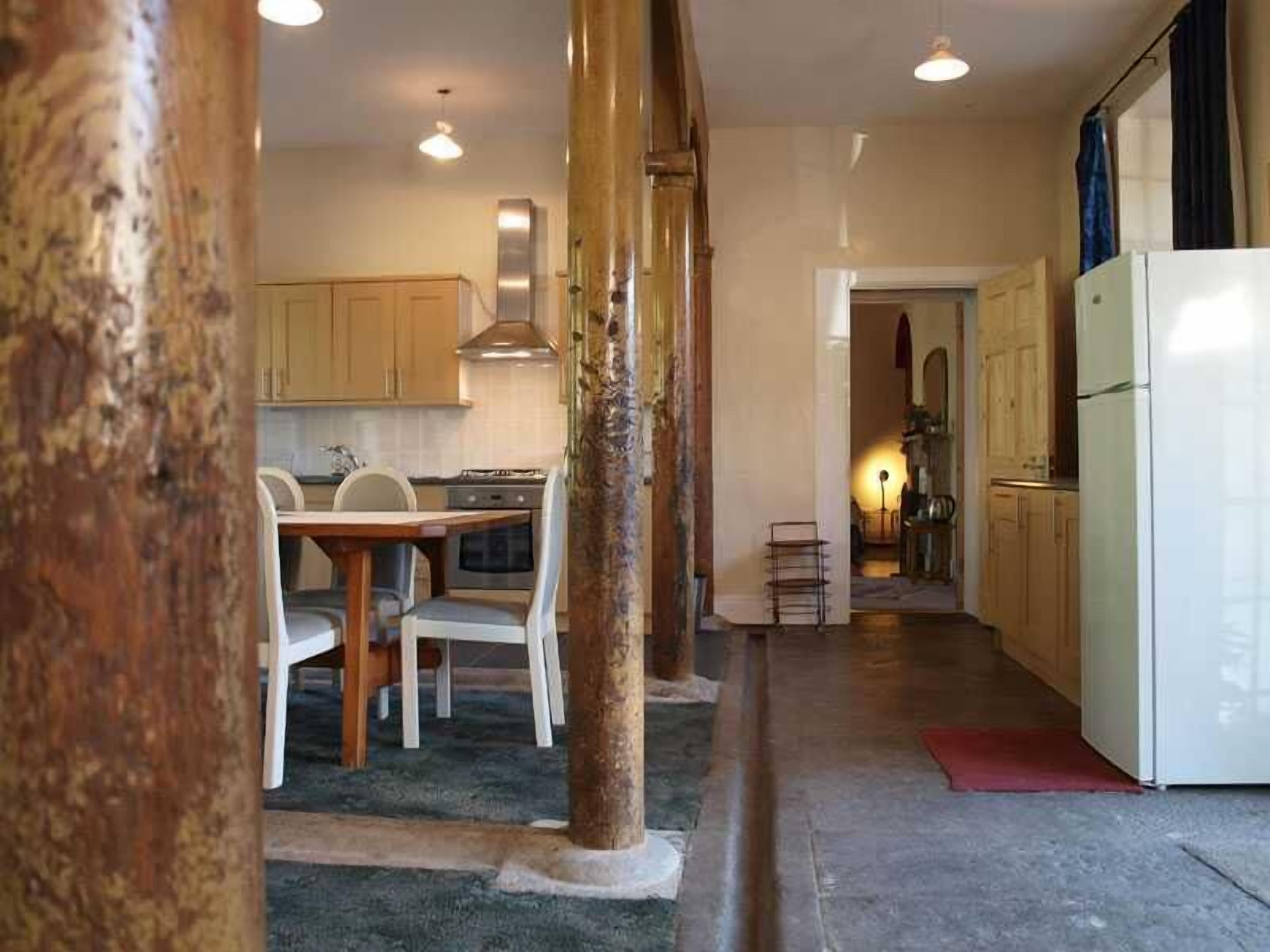 Une cuisine avec des meubles de rangement en bois, une table à manger avec des chaises, un réfrigérateur et un îlot central doté d’un évier.