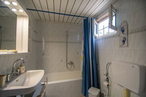 Un bagno con doccia, lavandino e WC. Si vede una finestra con tenda e uno specchio a parete.