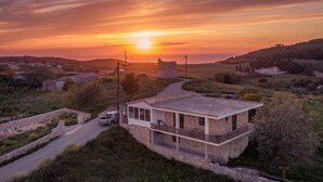 A modern house with a balcony, surrounded by a rural landscape and a sunset in the background. - Villa Windmill Sunset (Zakynthos)