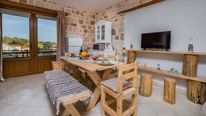 A dining area with a wooden table, chairs, and a bench. A television is mounted on the wall, and there is a window with curtains. - Villa Windmill Sunset (Zakynthos)