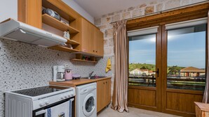 A compact kitchen with a washing machine, a stove, and a coffee maker. - Villa Windmill Sunset (Zakynthos)