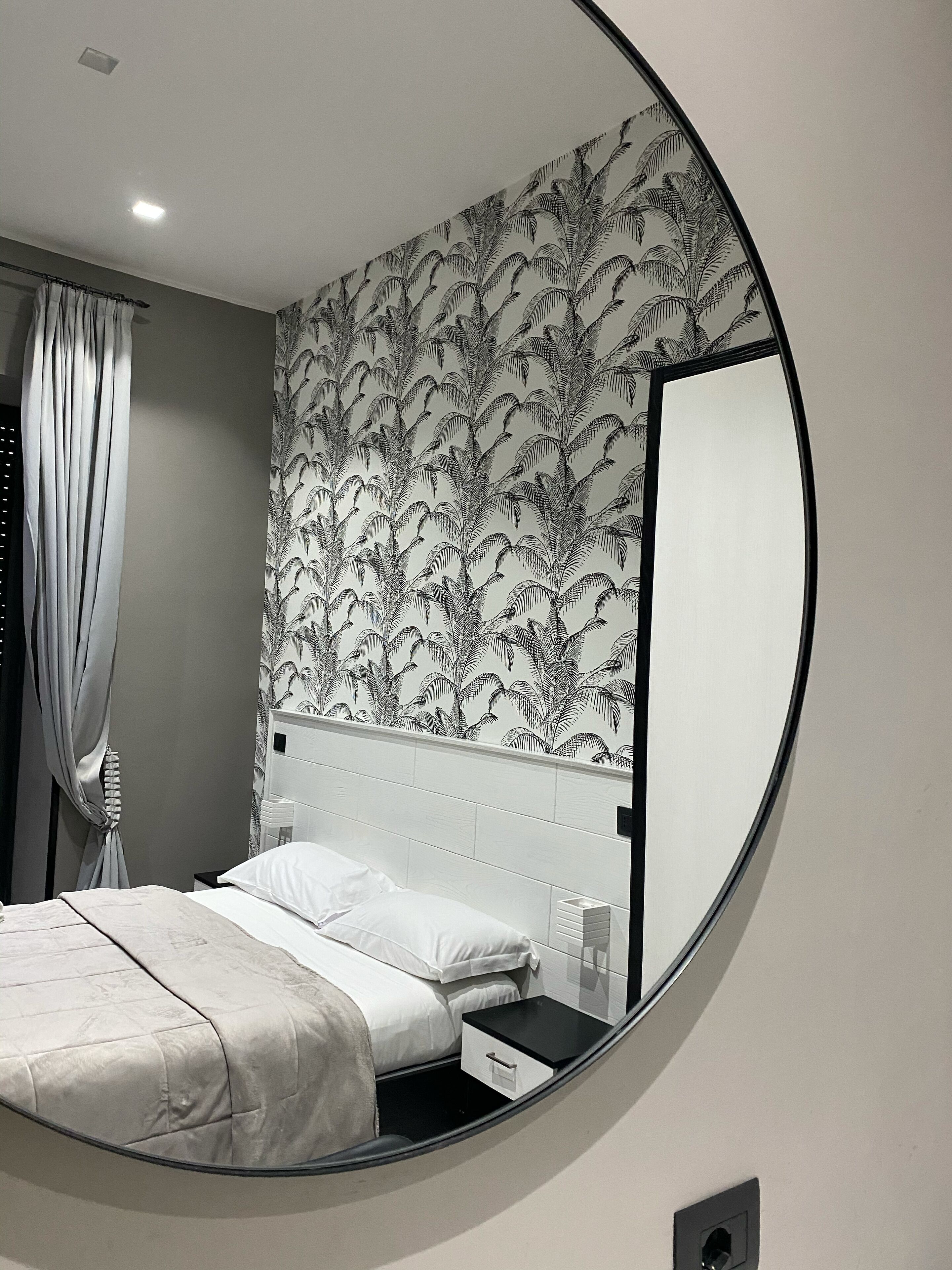 A bedroom with a bed, a nightstand, a mirror, and a wall with a leaf pattern.