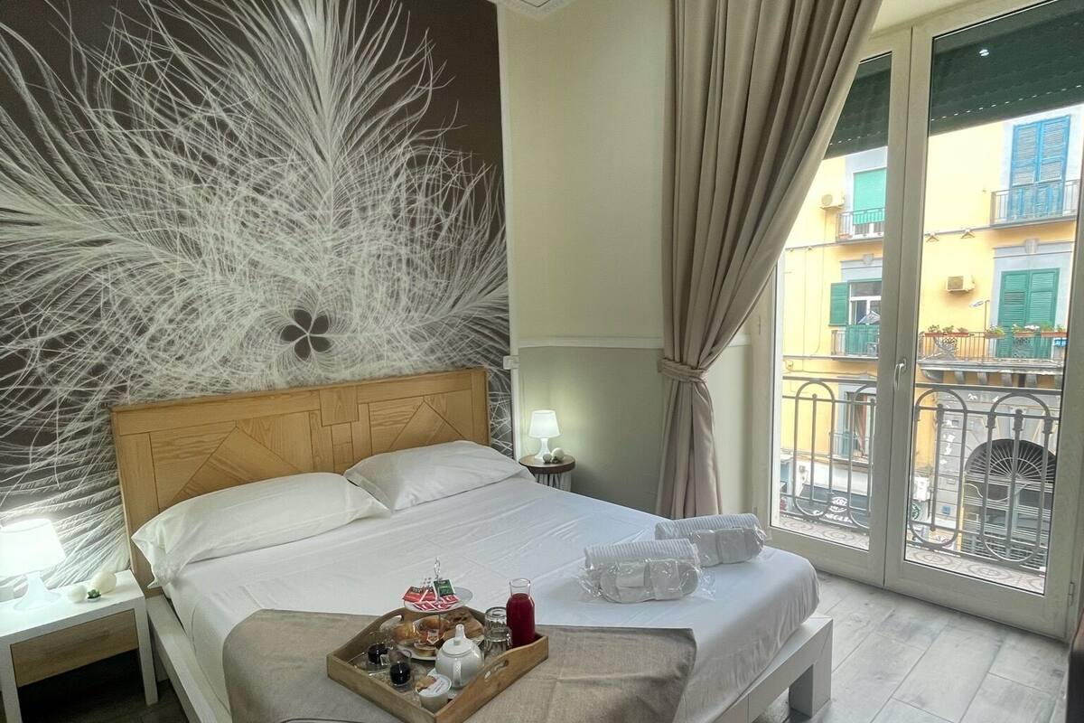 Una camera d'albergo con un letto, un vassoio con prodotti per la colazione, un comodino con una lampada e vista sul balcone esterno.