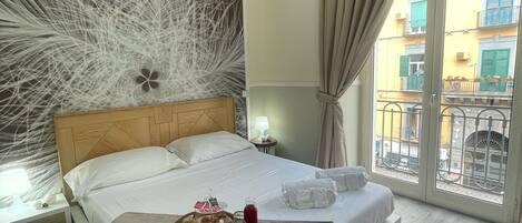 A hotel room with a bed, a tray of breakfast items, a nightstand with a lamp, and a view of the outside balcony.