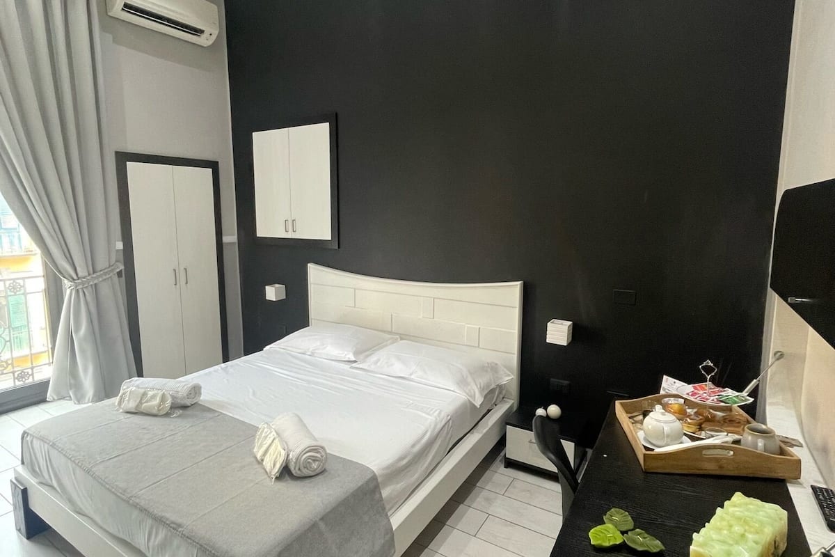 Una camera d'albergo moderna con un letto grande, un comodino con un vassoio per la colazione, una parete nera e una finestra con tende.