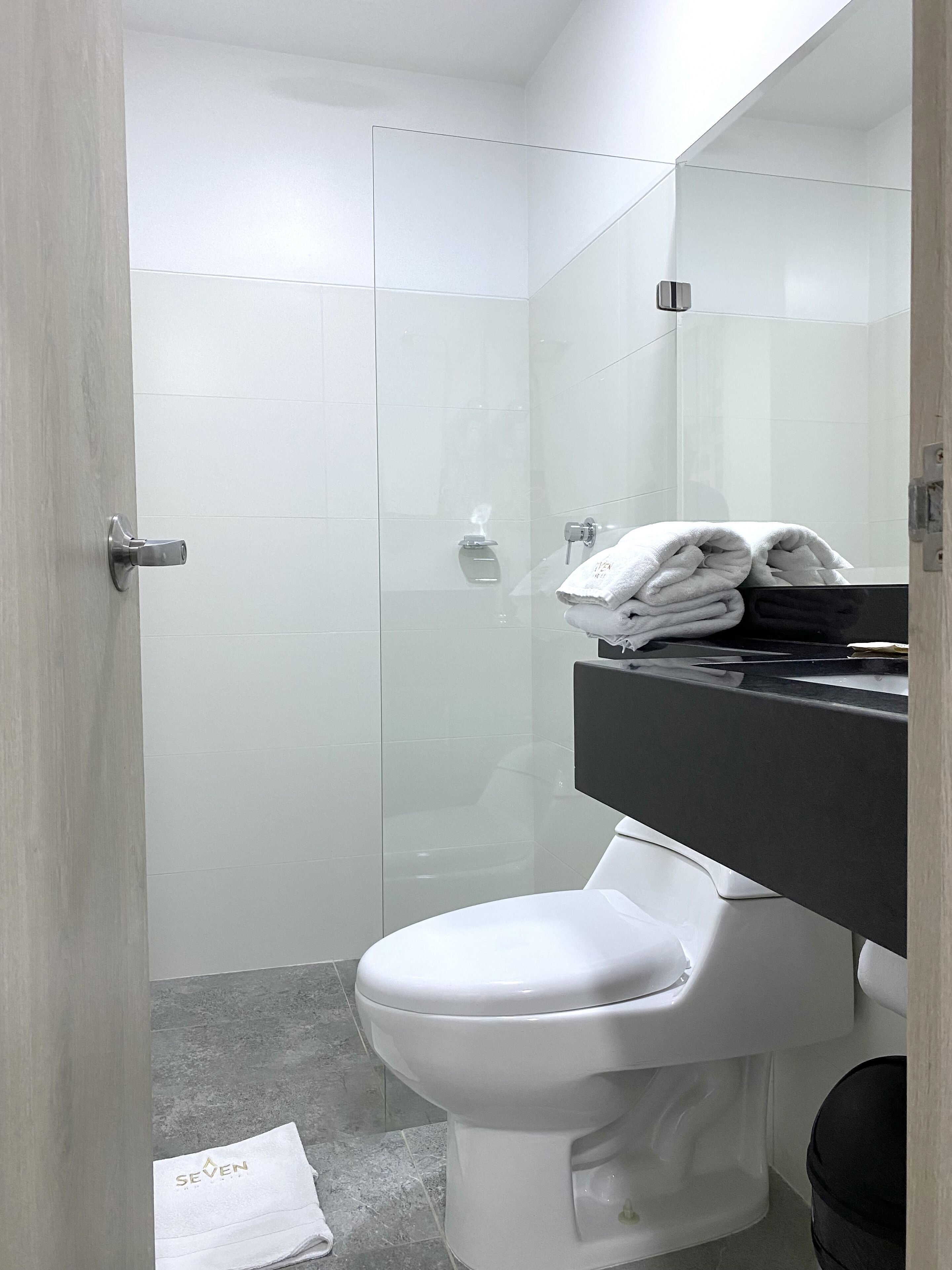 A bathroom with a toilet, a glass shower enclosure, and a sink with a towel stack.