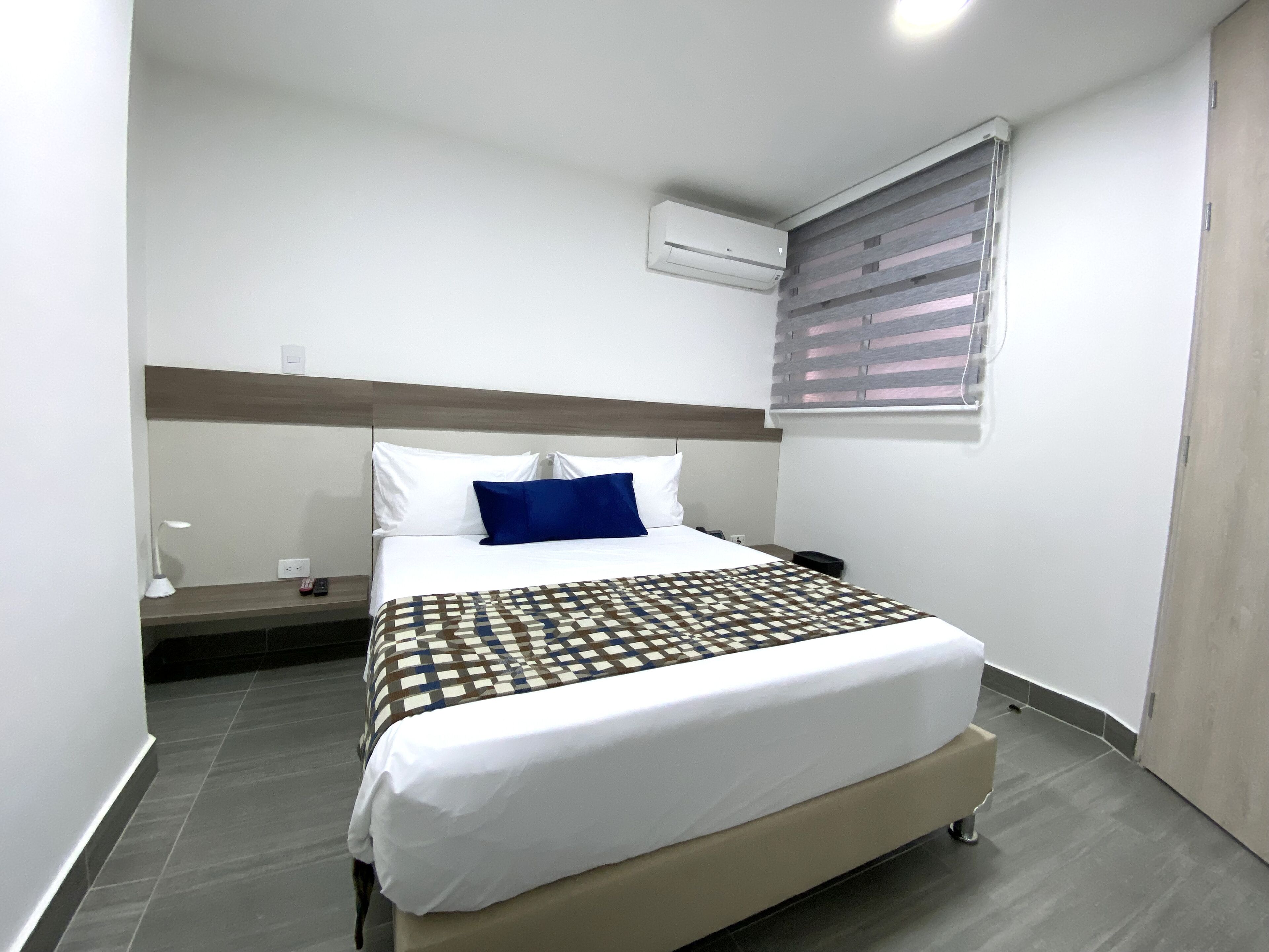 A neatly made bed with a patterned bedspread, a bedside lamp, and a wall-mounted air conditioner.