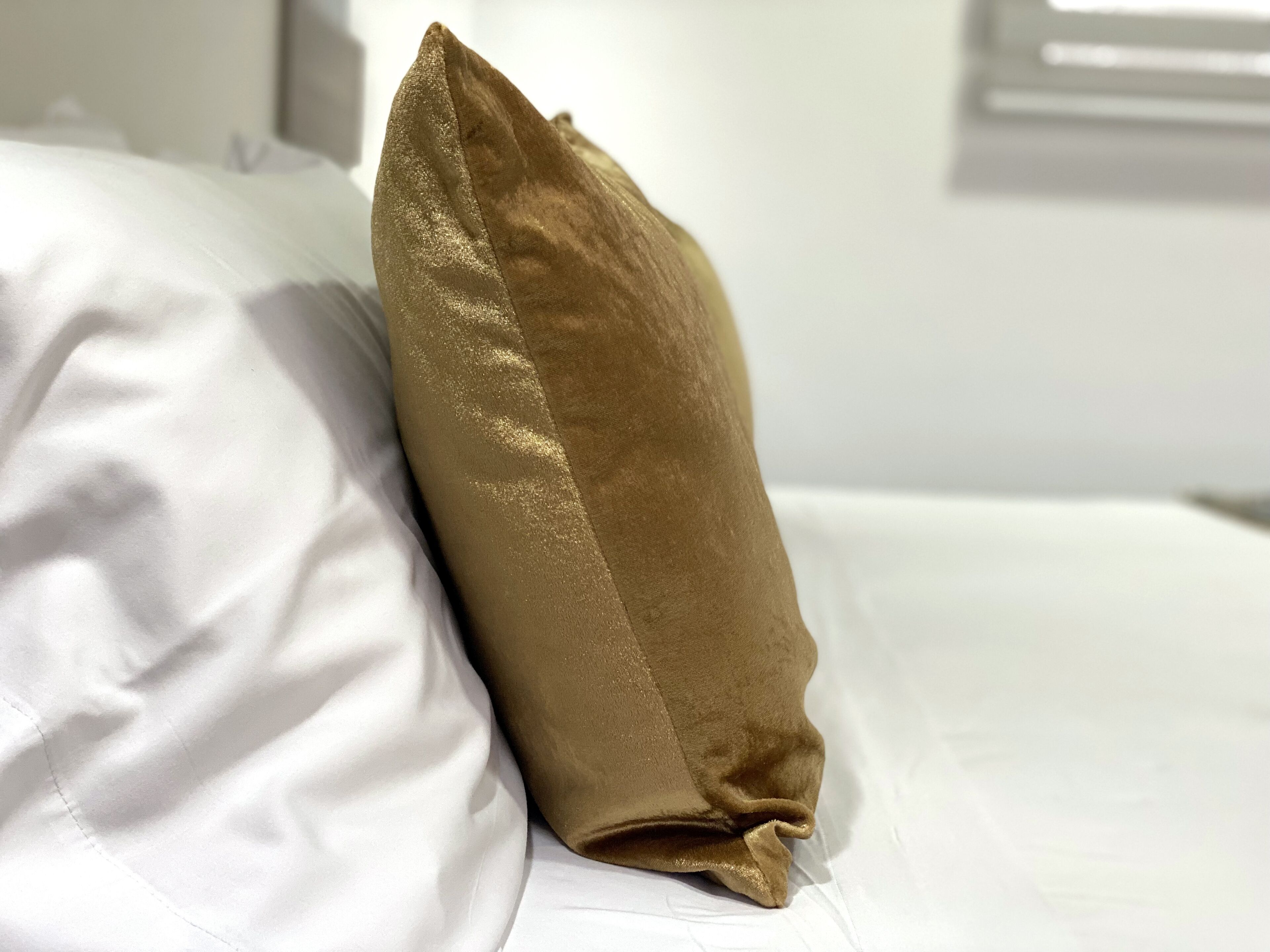 A bed with white sheets and a single gold-colored pillow.