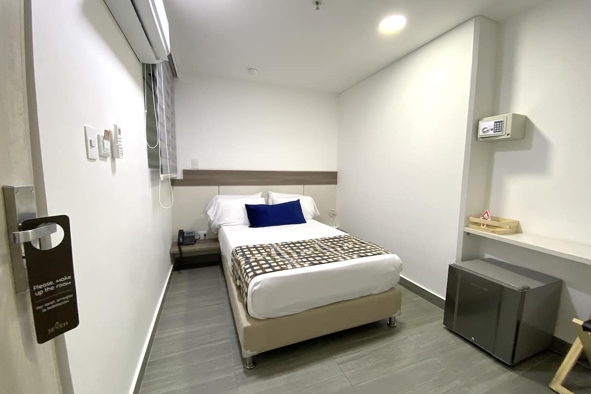 A hotel room with a bed, bedside table, and a small refrigerator.