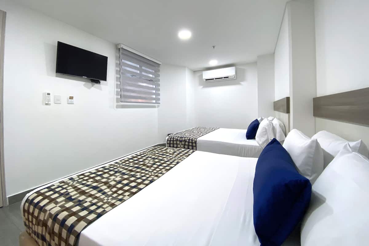 A hotel room with two beds, a TV, an air conditioning unit, and a window with blinds.