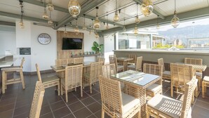 Ein Restaurant mit Korbmöbeln, Hängelampen, einer Uhr und Blick auf die Stadt.