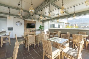 Un restaurante con mobiliario de mimbre, lámparas colgantes, un reloj y vistas de la ciudad.