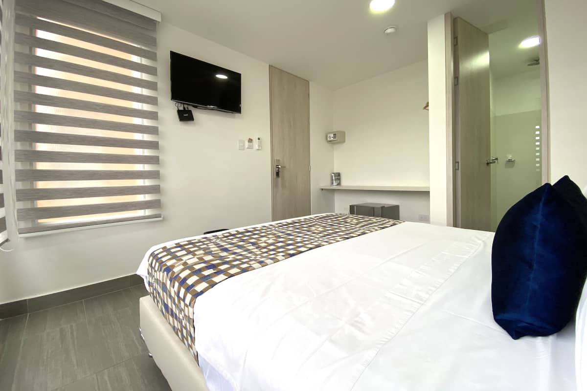 A modern hotel room with a large bed, a flat-screen TV mounted on the wall, a small bedside table, and a walk-in closet.