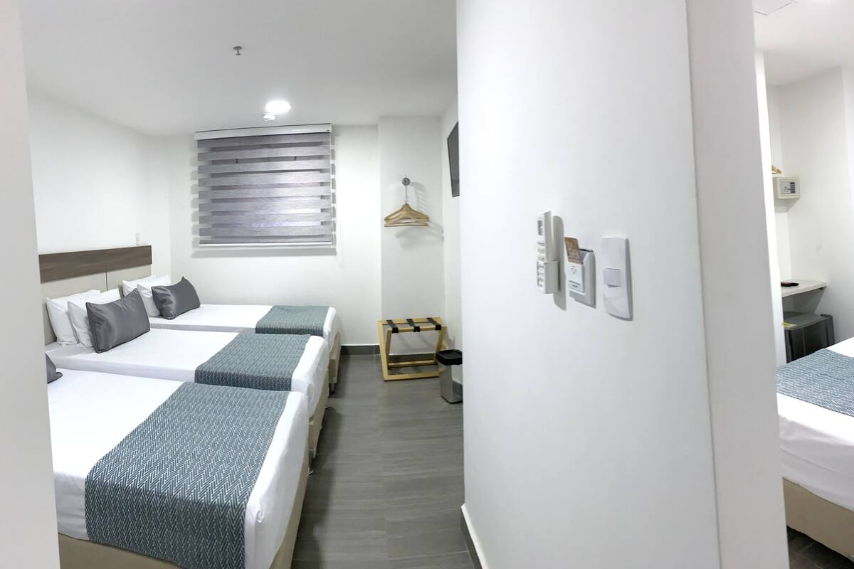 A hotel room with two single beds, a small desk, a chair, a hanging coat rack, and a window with blinds.