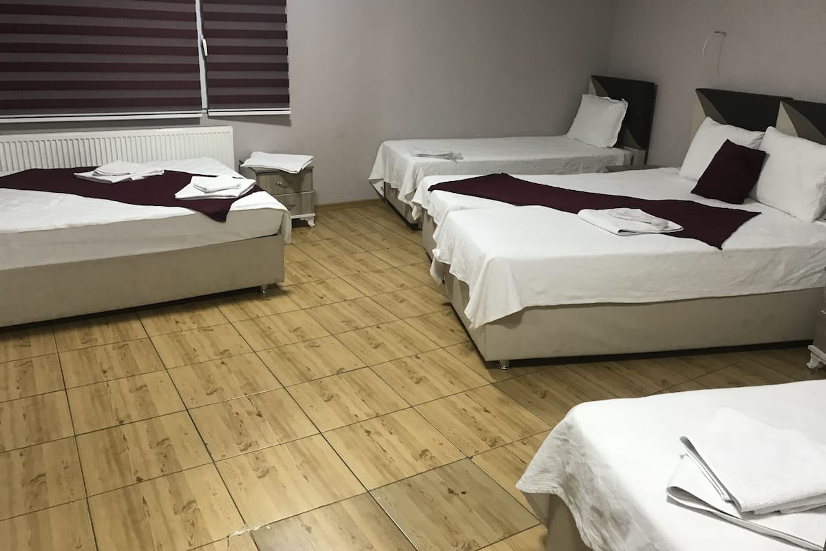 A hotel room with three beds, a small bedside table, and a window with blinds.