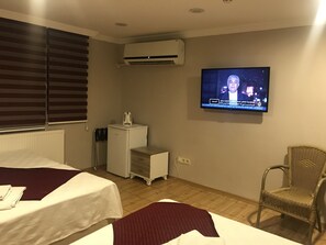 A hotel room with two beds, a television mounted on the wall, a small kitchenette, and a wicker chair. - Altinboynuz Family Hotel (Istanbul)