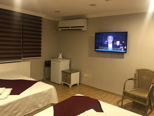 Quarto de hotel com duas camas, televisão presa na parede, pequena cozinha e uma cadeira de vime.