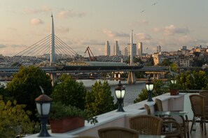 Vista para o rio com uma ponte moderna, área de refeições com mesas e cadeiras, e edifícios da cidade ao fundo.