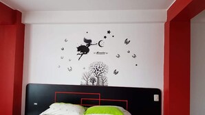 A bedroom with a bed, a wall decal of a fairy flying above a tree, and red and white walls. - Hostal El Parque (Huancayo)