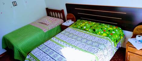 Un dormitorio con dos camas individuales, cada una con una colcha de diseño diferente. La habitación tiene un cabecero de madera, una mesita de noche pequeña de madera y una pared con adornos adhesivos.