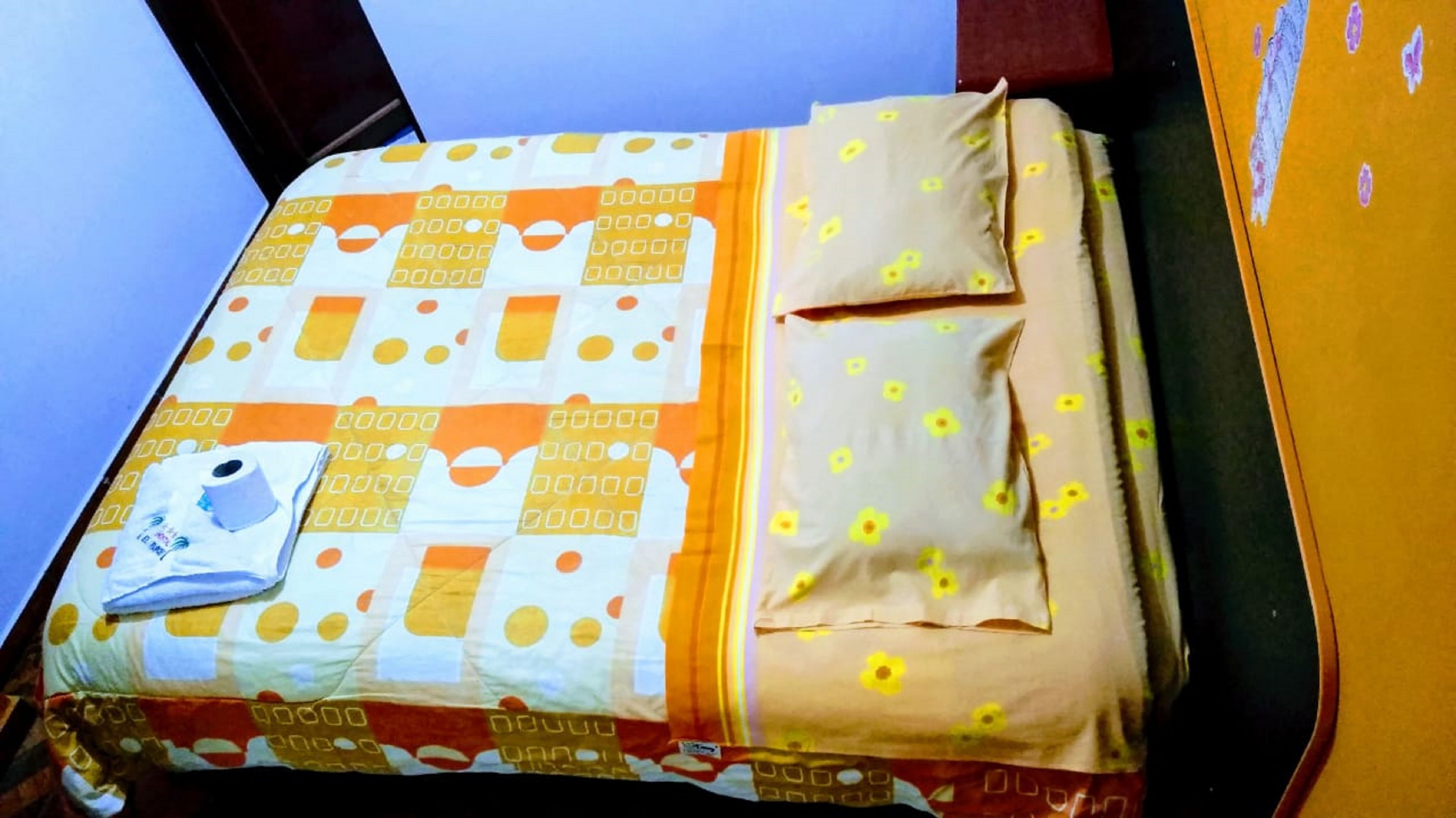 A bed with a patterned bedspread, pillows, and a rolled-up towel.