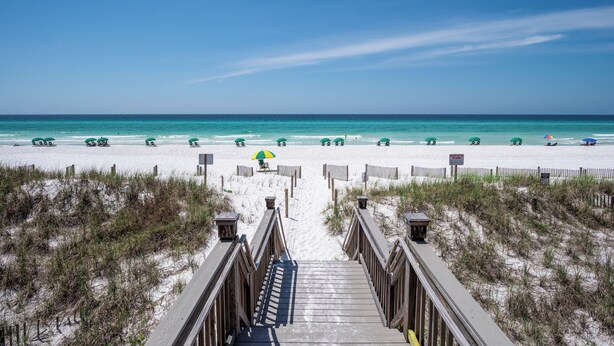 A beach with a wooden boardwalk leading to the water, surrounded by sand dunes.