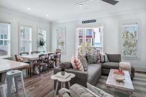 Amplia sala de estar con una mesa de comedor, un sofá y una mesa de centro. Se ve un letrero que dice "BEACH HOUSE".