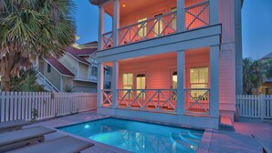 A two-story house with a swimming pool, white picket fence, and a balcony with a railing.